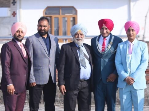 Group of Punjabi men in traditional attire and suits, posing outdoors.