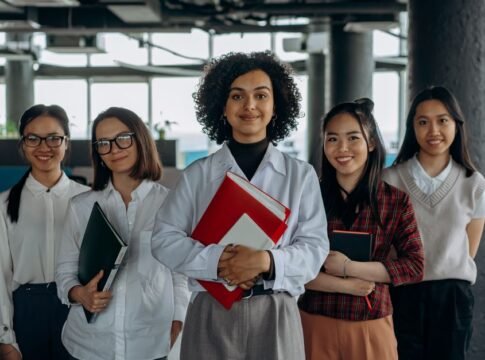 Group of diverse women colleagues smiling in a modern office setting, holding documents. Group of diverse women colleagues smiling in a modern office setting, holding documents.
