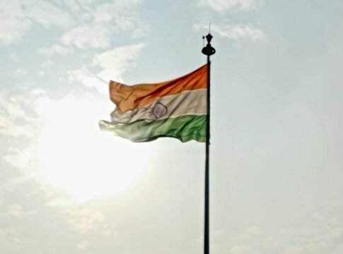 Indian national flag waving on flagpole against a bright sky with clouds.