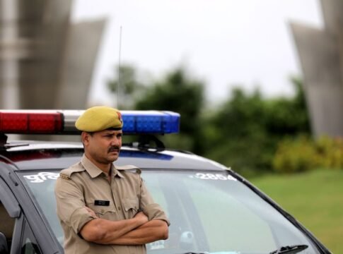 Indian police officer with arms crossed standing by a patrol car outdoors, showcasing authority and law enforcement presence.