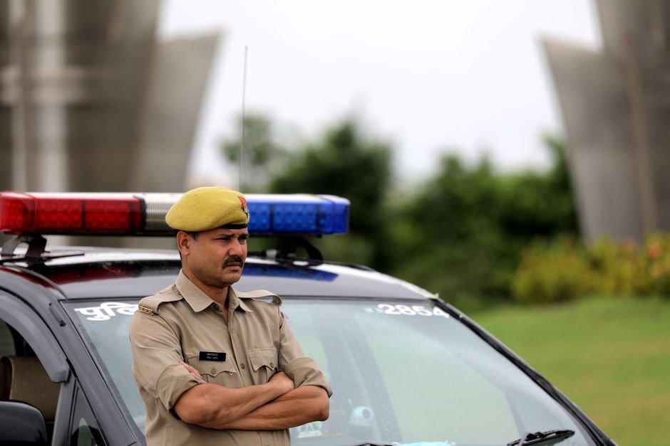 Madhya Pradesh DGP Intervenes, Resolves Harassment of Kashmiri Pharmacy Students in Bhopal Indian police officer with arms crossed standing by a patrol car outdoors, showcasing authority and law enforcement presence.