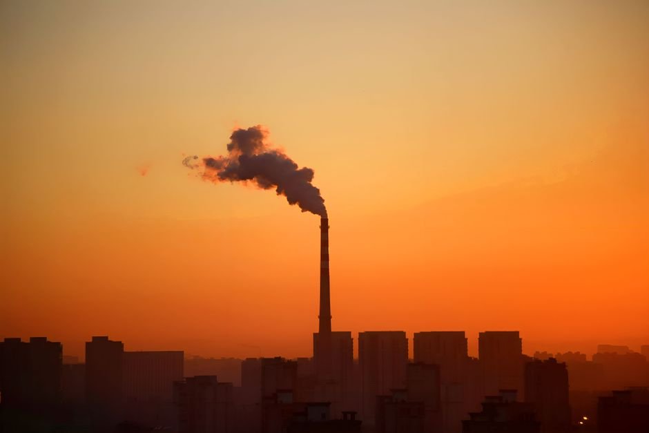 Delhi Implements Construction Ban to Combat Winter Air Pollution Industrial smokestack emitting smoke during sunset, highlighting environmental impact.
