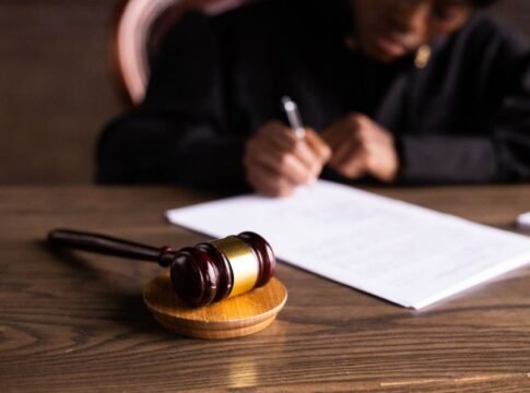 Judge signing documents at desk with focus on gavel, representing law and justice.