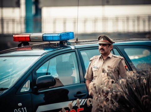 Male in uniform standing near patrol car with flashing lights and looking away Male in uniform standing near patrol car with flashing lights and looking away