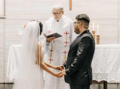 Newlyweds hold hands during a church ceremony led by a priest. Newlyweds hold hands during a church ceremony led by a priest.