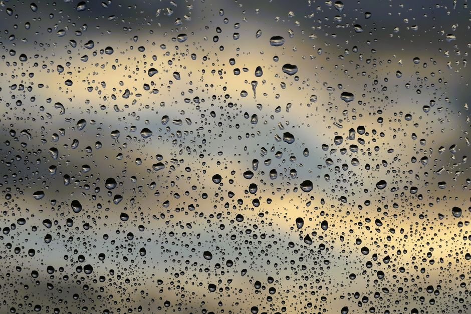 Himachal Pradesh Faces Road Blockades, Power Outages Amidst Persistent Rainfall Raindrops scattered on a window pane with a soft, cloudy sky in the background, creating a moody atmosphere.