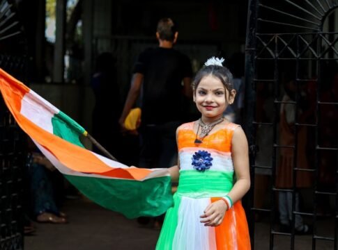 Smiling girl in tricolor dress holds Indian flag during Independence Day celebration in India.