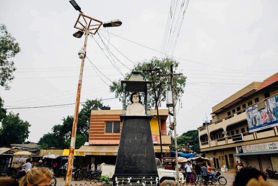 Uttar Pradesh: Mayawati Calls for Local Resolution of Hijab Row, Cites Ambedkar’s Constitution Street view of a bust sculpture in an Indian town square, surrounded by buildings and people.