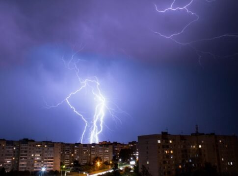 Striking lightning bolt illuminates cityscape during a nighttime thunderstorm.