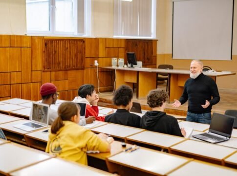 Students engaging with a professor in a university lecture hall, utilizing technology. Students engaging with a professor in a university lecture hall, utilizing technology.