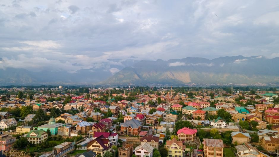 Jammu and Kashmir Braces for Continued Hot, Humid Weather with Scattered Showers Through August Stunning aerial view of colorful Srinagar city with Himalayan backdrop under cloudy skies.