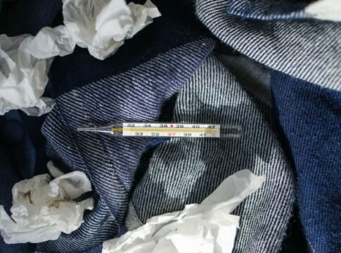 Thermometer with crumpled tissues on denim fabric, evoking themes of sickness and care.