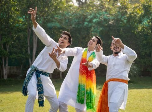 Three men in traditional clothing celebrate outdoors with energetic joy and colorful scarves.