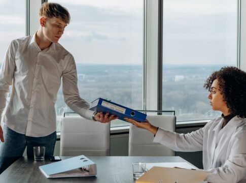 Two colleagues exchange documents in a contemporary office with a scenic city view. Two colleagues exchange documents in a contemporary office with a scenic city view.