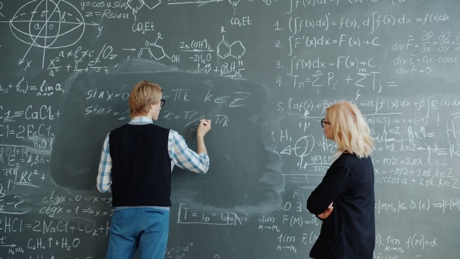 Ramban School Zonation Sparks Concern; Plus-Two Lecturers Demand Verification Two professors collaborate on solving complex math equations in classroom.