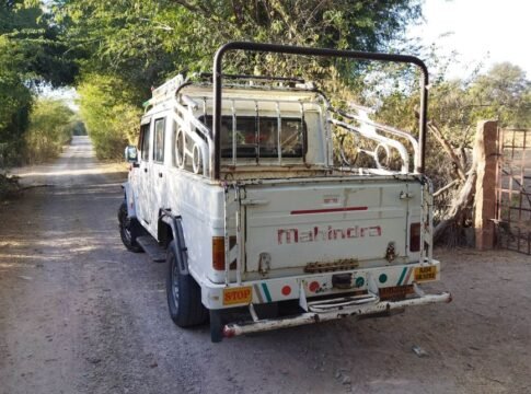 White Mahindra vehicle parked on a dirt road amidst green trees, captured in daylight. White Mahindra vehicle parked on a dirt road amidst green trees, captured in daylight.
