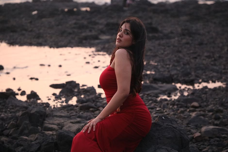 Punjab-Born Pallavi Mukhija Crowned Mrs Canada World 2026 Woman in a red dress sitting on rocks by the beach during sunset, evoking elegance and tranquility.
