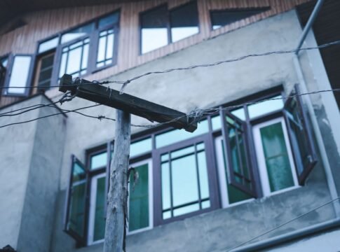 Wooden power pole with electricity wires against an urban building with open windows in Srinagar. Wooden power pole with electricity wires against an urban building with open windows in Srinagar.