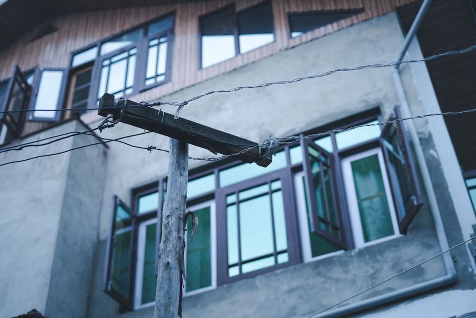 Jammu and Kashmir: KPDCL Announces Scheduled Power Shutdowns Across Kashmir Division Wooden power pole with electricity wires against an urban building with open windows in Srinagar.