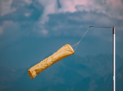 Yellow windsock blowing in the wind, mounted on a pole against a cloudy blue sky. Yellow windsock blowing in the wind, mounted on a pole against a cloudy blue sky.