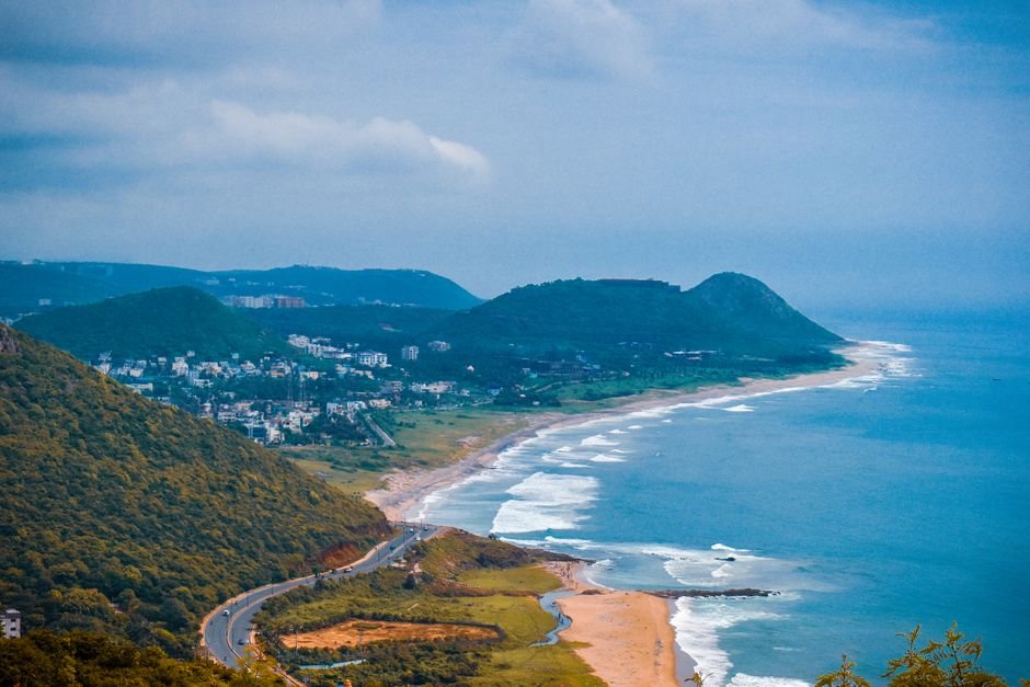 Andhra Pradesh Hospitality Sector Seeks Land Allocation to Boost Budget Tourism A breathtaking aerial view of the coastline in Visakhapatnam, capturing lush hills and the vibrant sea.