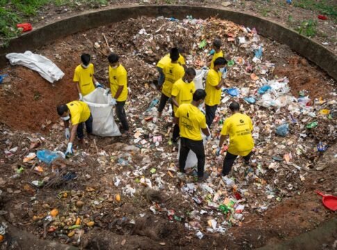 A group of volunteers in yellow shirts clean up a large waste pit outdoors, demonstrating teamwork and environmental care. A group of volunteers in yellow shirts clean up a large waste pit outdoors, demonstrating teamwork and environmental care.