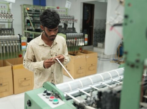 A man focuses on operating a machine in a textile factory, surrounded by large industrial equipment. A man focuses on operating a machine in a textile factory, surrounded by large industrial equipment.