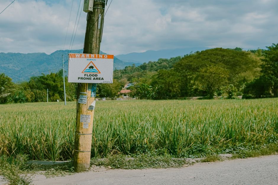 Southeast Asia Urged to Enhance Early Warning Systems for Vulnerable Groups A rural scene with a flood warning sign against a mountainous backdrop.
