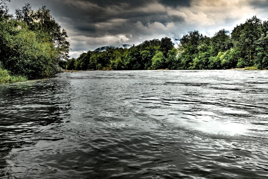 Andhra Pradesh Authorities Issue Alert as Sabari River Swells Amid Heavy Rains A scenic river view surrounded by lush trees under moody skies.