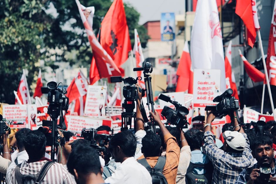 Tamil Nadu Declares Public Holiday on October 6 for Bypolls in Madurantakam and Dharapuram A vibrant protest in Chennai, India with media coverage featuring bright red flags and banners.