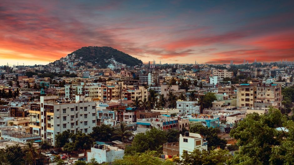 A vibrant sunset paints the sky over the bustling cityscape of Visakhapatnam, India.