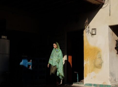 A woman wearing a headscarf walks past a graffiti wall. Low light, artistic scene.