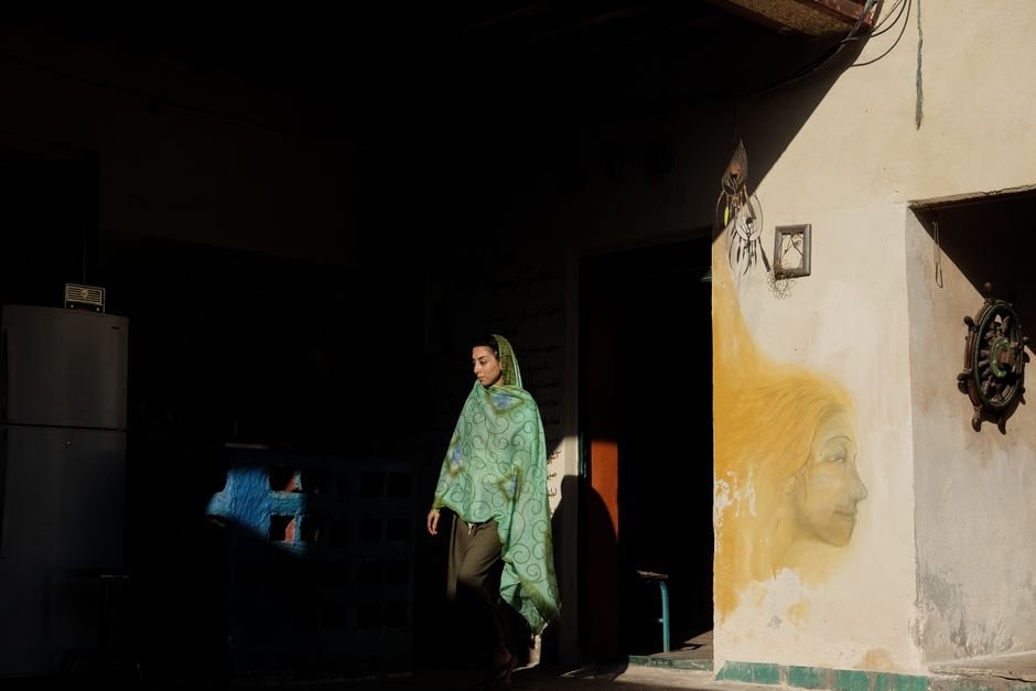 A woman wearing a headscarf walks past a graffiti wall. Low light, artistic scene.