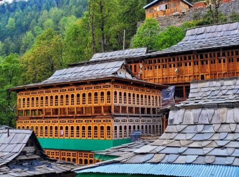 Charming wooden structures in a quaint Himachal Pradesh village surrounded by lush greenery.