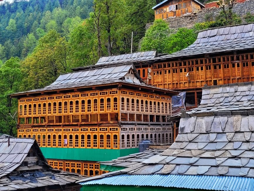 Charming wooden structures in a quaint Himachal Pradesh village surrounded by lush greenery.