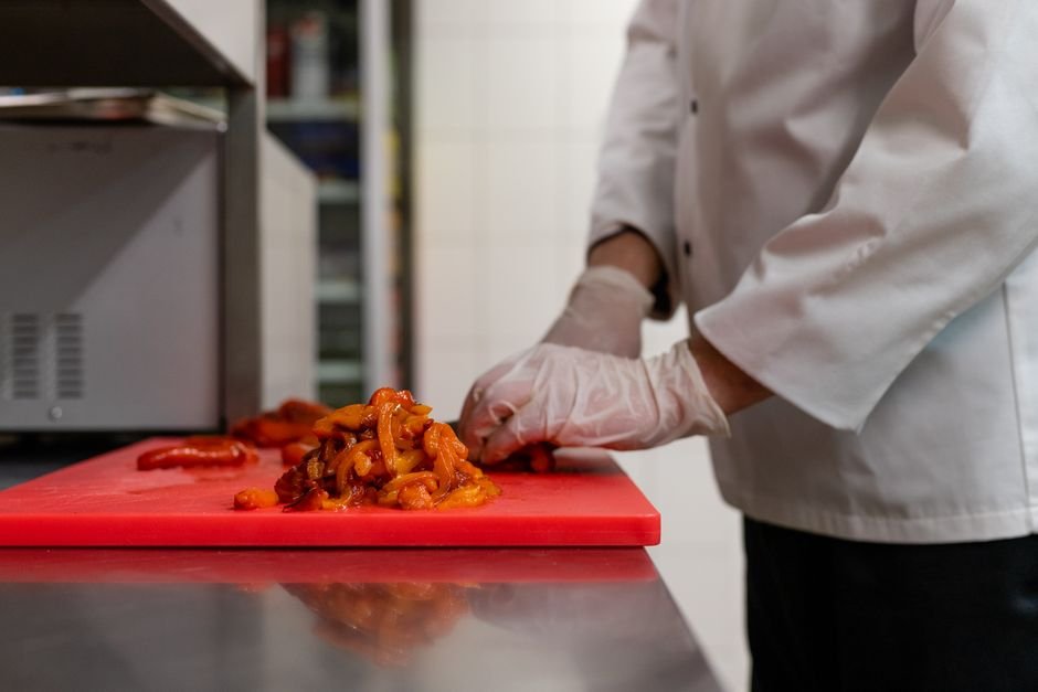 Jammu & Kashmir FDA Bans Four Ghee Brands for Failing Food Safety Standards Chef chopping vegetables on a red cutting board in a professional kitchen.