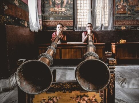 Concentrated Tibetan monks wearing traditional playing ceremonial melody on huge dungchen horns in Buddhist temple