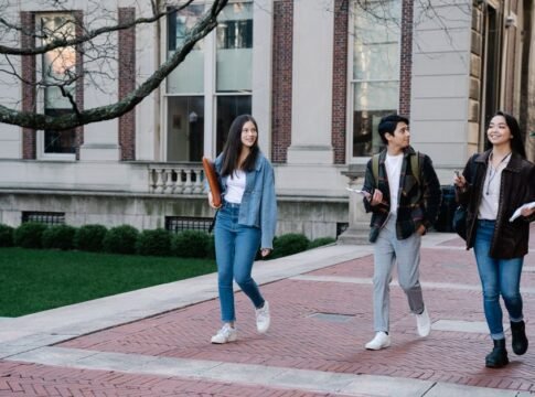 Group of young students walking on campus sidewalk on a bright day, showcasing casual university life.