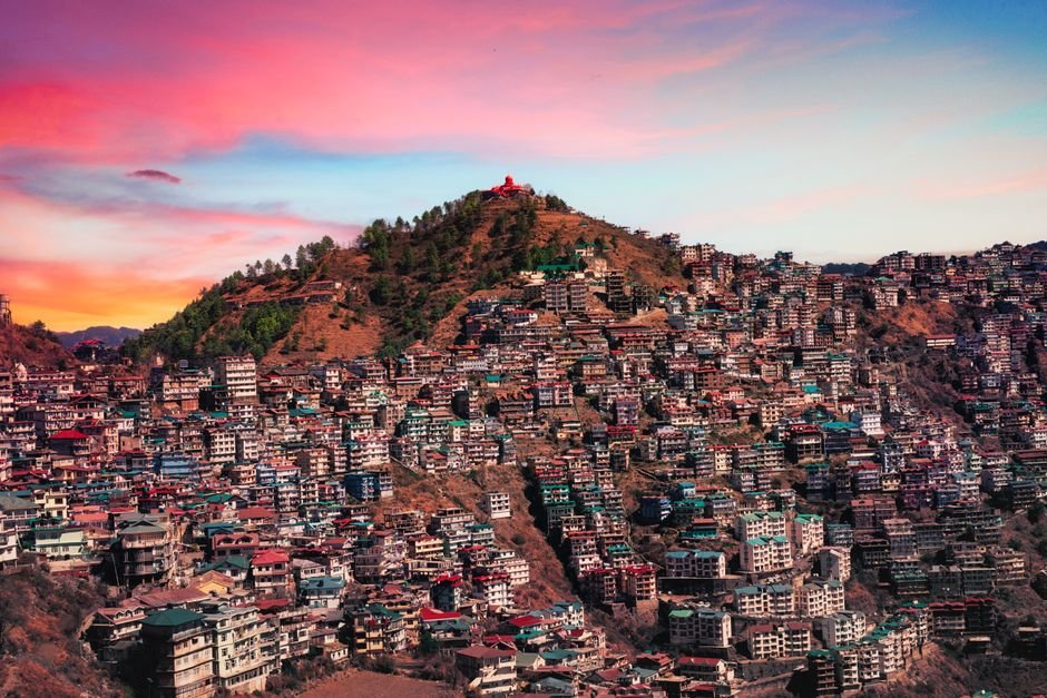 Himachal Pradesh: ‘Far From Home’ Tops Awards at Shimla International Film Festival Majestic aerial view of Shimla, India with colorful buildings against a vibrant sunset sky.