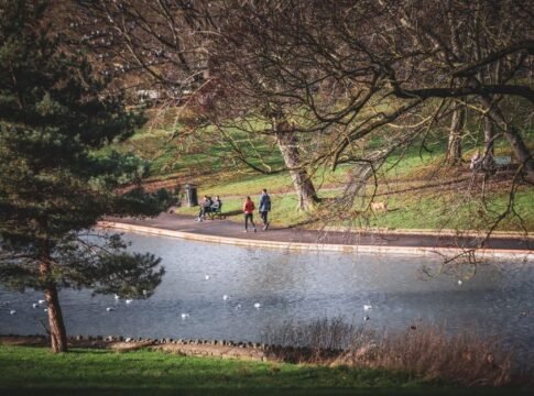 People enjoying a leisurely walk by a pond in a Bristol park. Scenic view with trees and ducks. People enjoying a leisurely walk by a pond in a Bristol park. Scenic view with trees and ducks.
