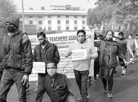 Protesters march for teachers' rights, holding banners in an urban setting.