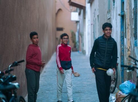Three teenagers walk through a narrow alley in the Medina of Essaouira, Morocco.