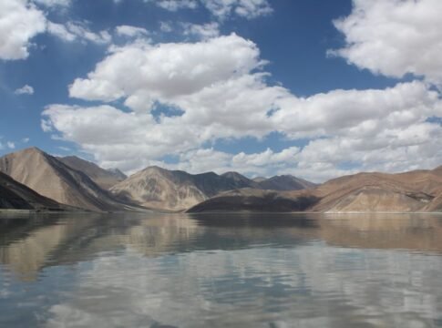 Tranquil mountain lake reflecting a clear blue sky with clouds.