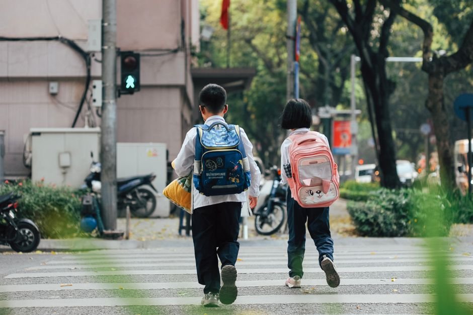 Delhi Students Navigating Major Roads Alone Amidst Safety Concerns: Study Two children with backpacks crossing a street at a pedestrian crossing.
