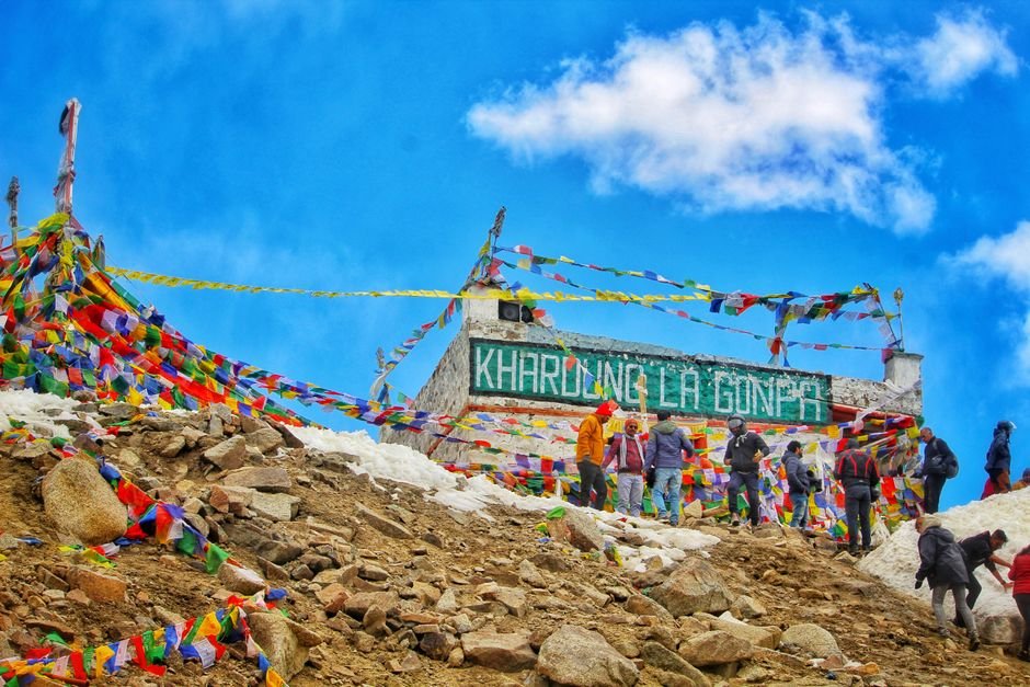 Kashmir’s Dr. Mushtaq Ahmad Malla Conquers 72-km Khardung La Ultra-Marathon Vibrant scene of Khardung La Pass with people and prayer flags in Ladakh, India.