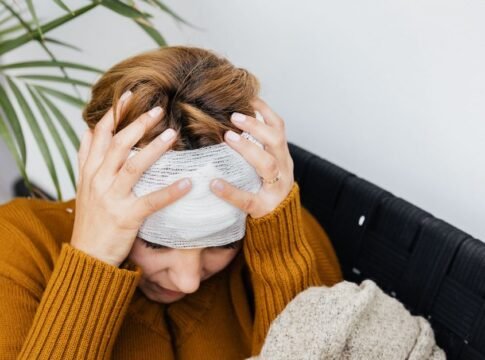 Woman with head injury holding her head in pain indoors.