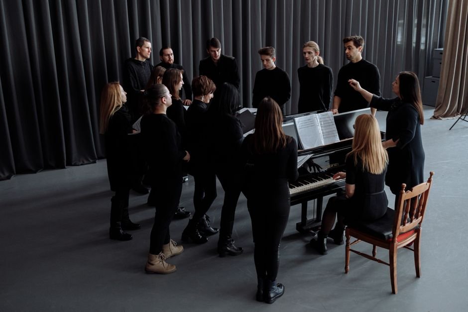 InterTalent Agency Elevates Dejah McCombe and Lucy Bendien to Co-Heads of Creator Division A choir group rehearsing indoors with a conductor and pianist, creating a musical harmony.