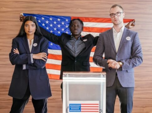 A group of diverse individuals standing confidently in front of an American flag at an election podium.