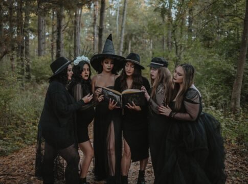 A group of women in witch costumes reading a spell book amidst an enchanting forest.