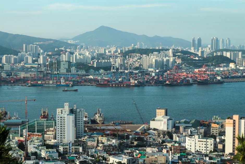 Kore-eda Hirokazu Reflects on Directing Children, Citing Loach and Hou as Influences A scenic view of Busan city with skyscrapers and busy harbor under clear skies.